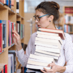 Woman browsing a library shelf holding a stack of books
