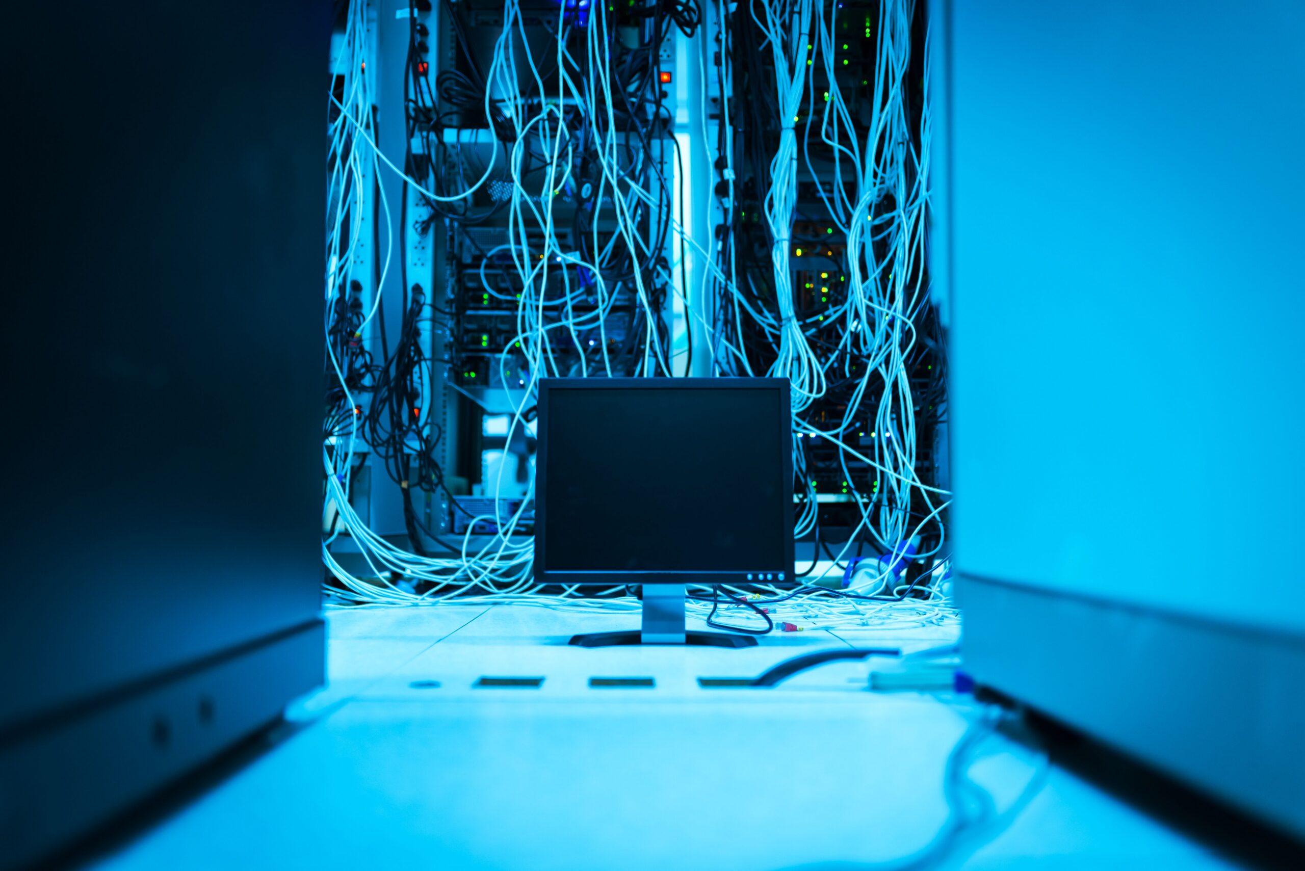 computer monitor in front of wires with blank walls on the sides. Whole image is toned blue.